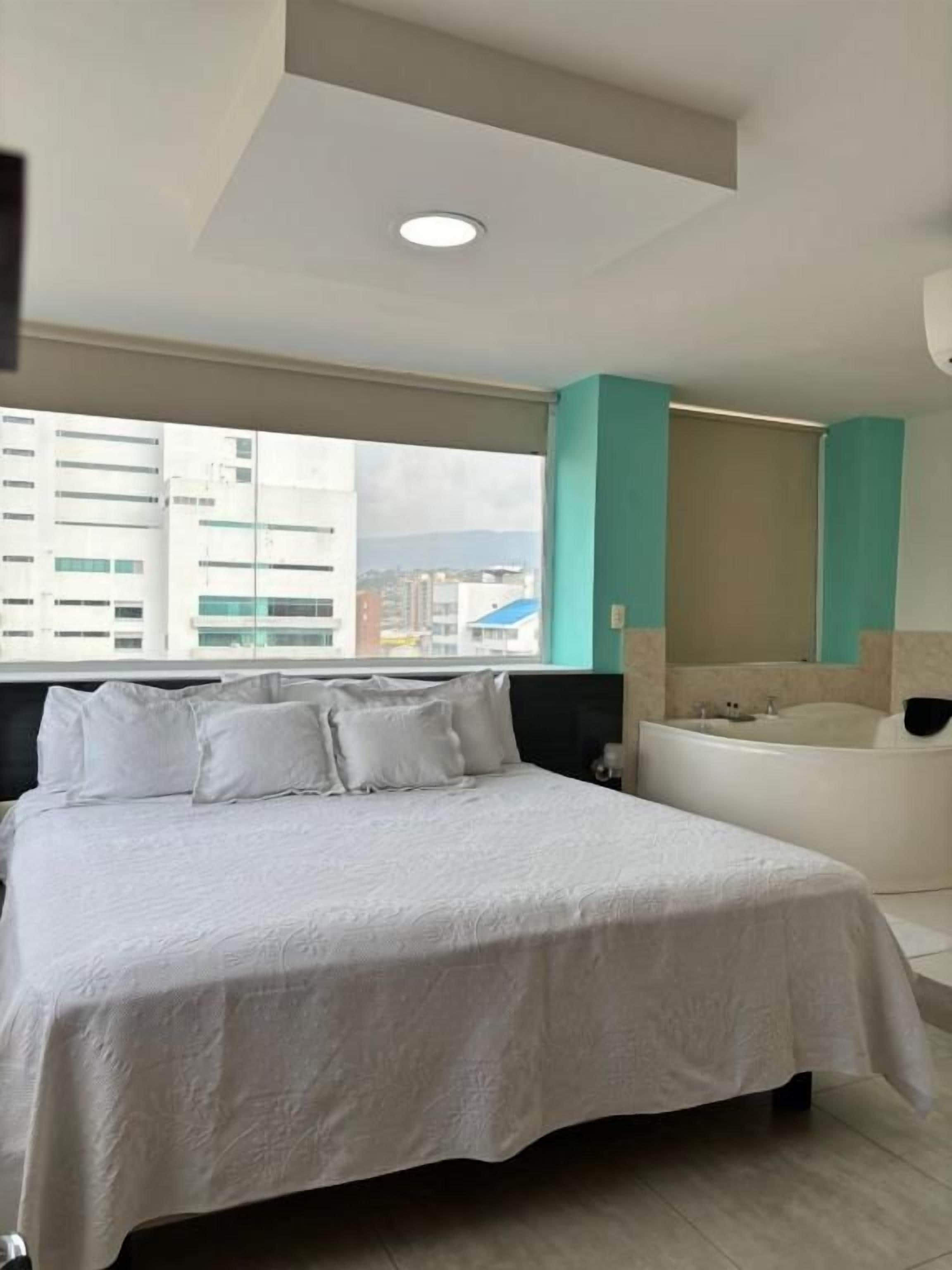 Une chambre d’hôtel dotée d’un grand lit, d’une fenêtre donnant sur la ville, d’une baignoire et présentant un design moderne.