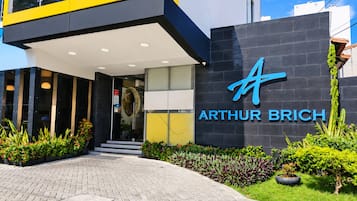 A modern hotel entrance with a prominent logo, a covered walkway, and well-maintained landscaping.