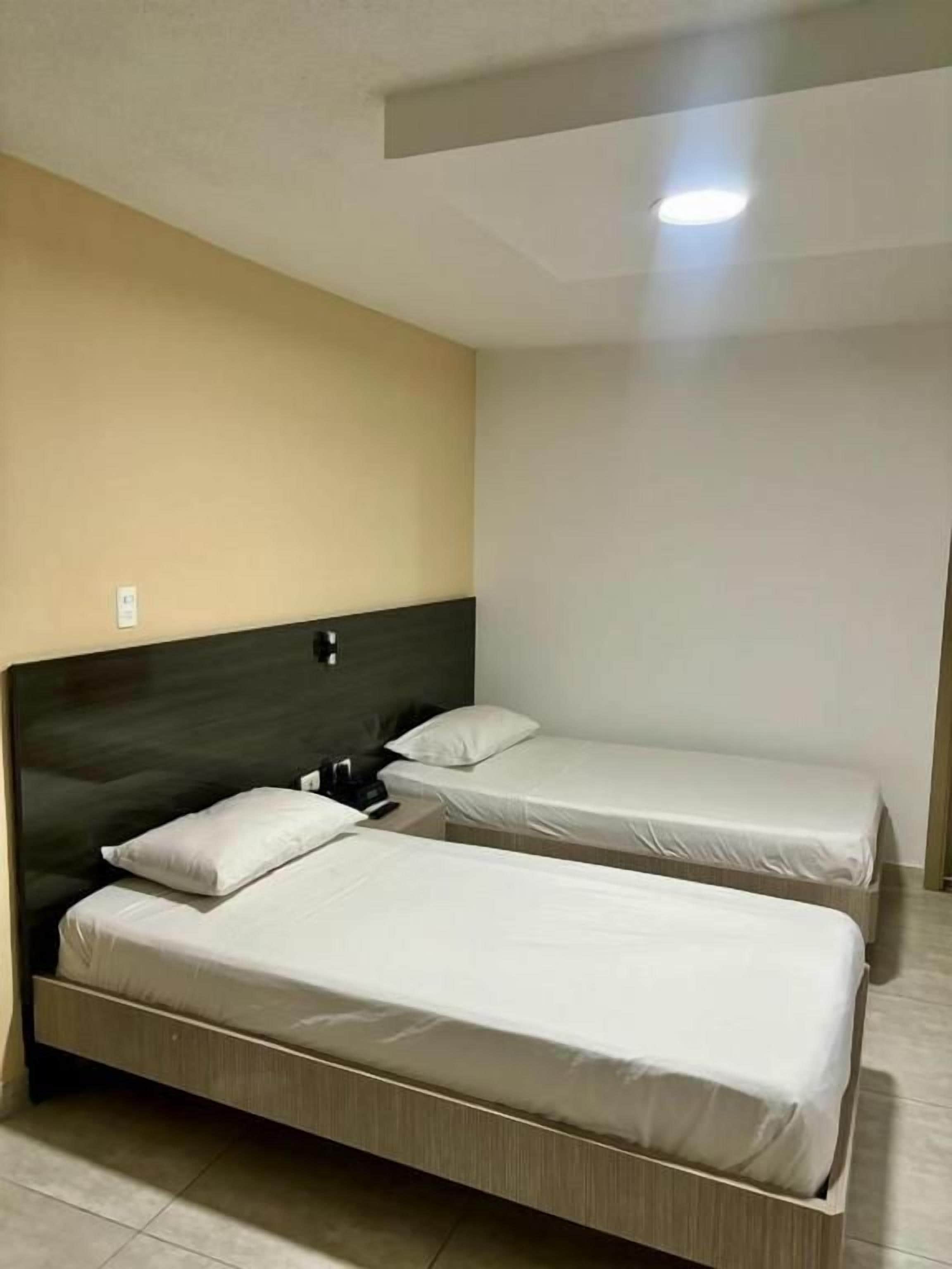 A hotel room with two single beds, a dark headboard, and a light-colored wall.