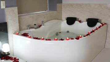 A modern bathroom with a large bathtub, a mirror, and a small table with a candle.