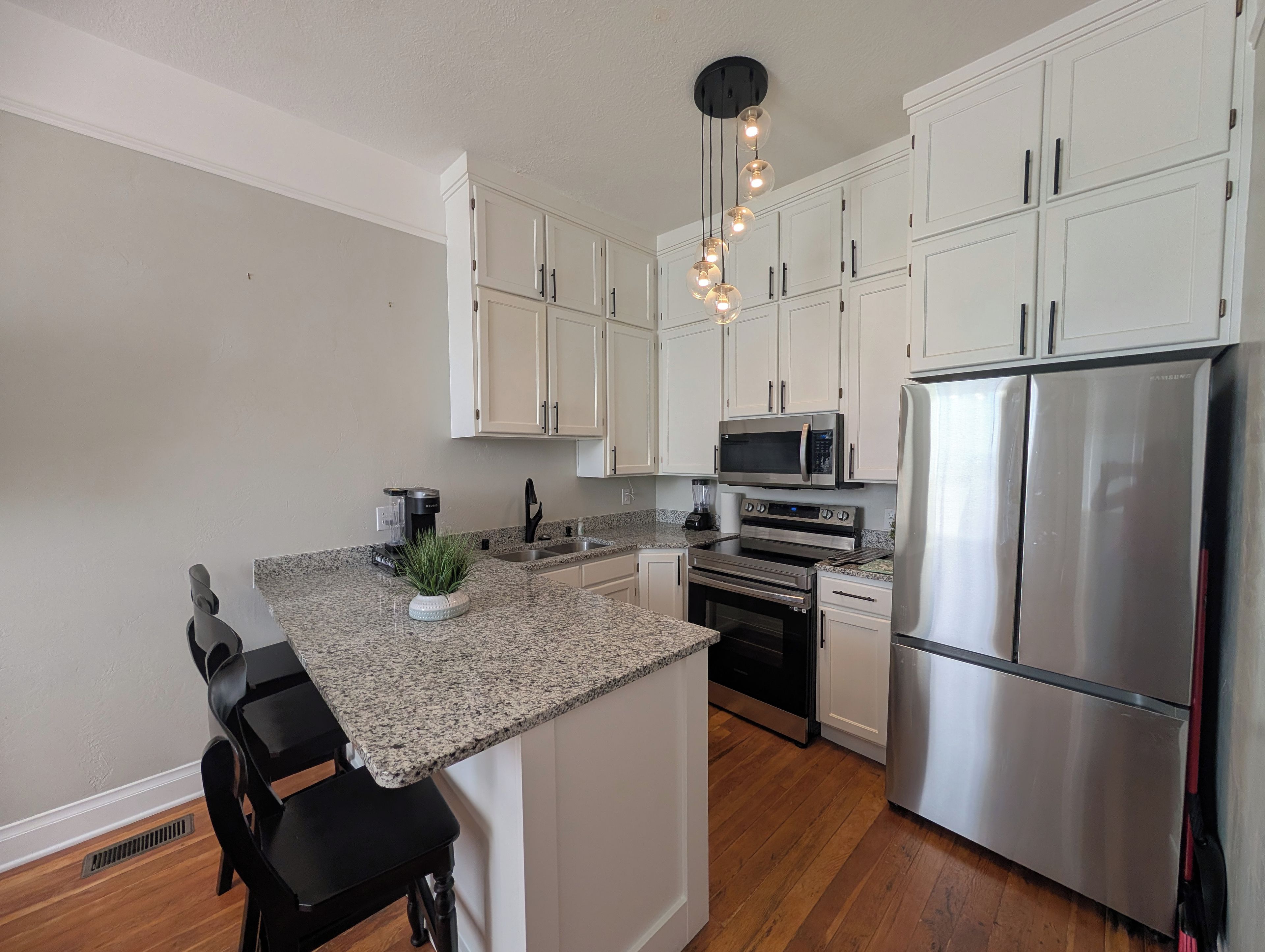 A modern kitchen with white cabinets, stainless steel appliances, a granite countertop, and a black bar stool.