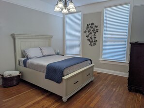 A bedroom with a bed, bedside tables, a wall decoration, and a window with blinds.