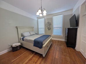 A bedroom with a bed, a dresser, a television, and a wall-mounted light fixture.