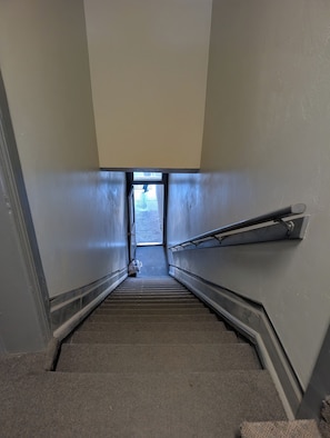 A narrow stairway with a handrail on one side and a door at the top.