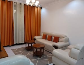 Una sala de estar con un sofá, dos mesitas redondas de madera y una alfombra estampada.