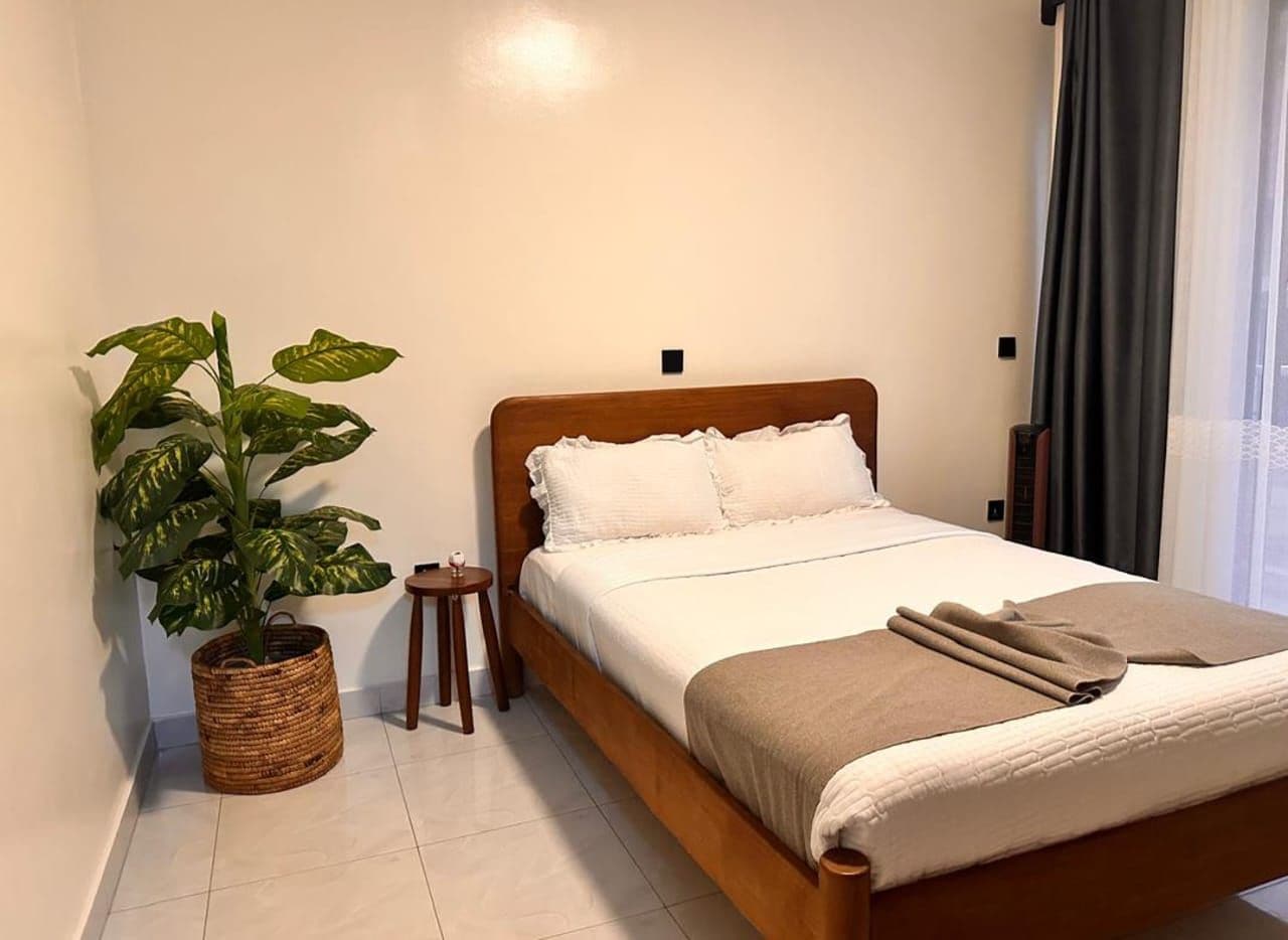 A neatly made bed with a wooden headboard, a potted plant, and a small table beside it.