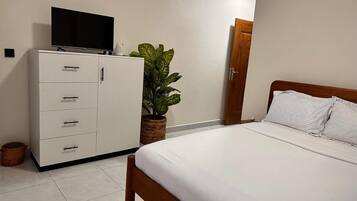 A bedroom with a bed, a TV on a cabinet, and a potted plant.