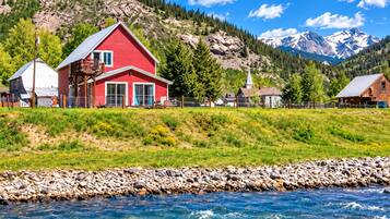 A red house with a balcony, a church, and mountains in the background.