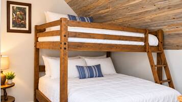 Un lit superposé avec une structure en bois et une literie blanche, une petite table de chevet avec une lampe et un tableau encadré au mur.