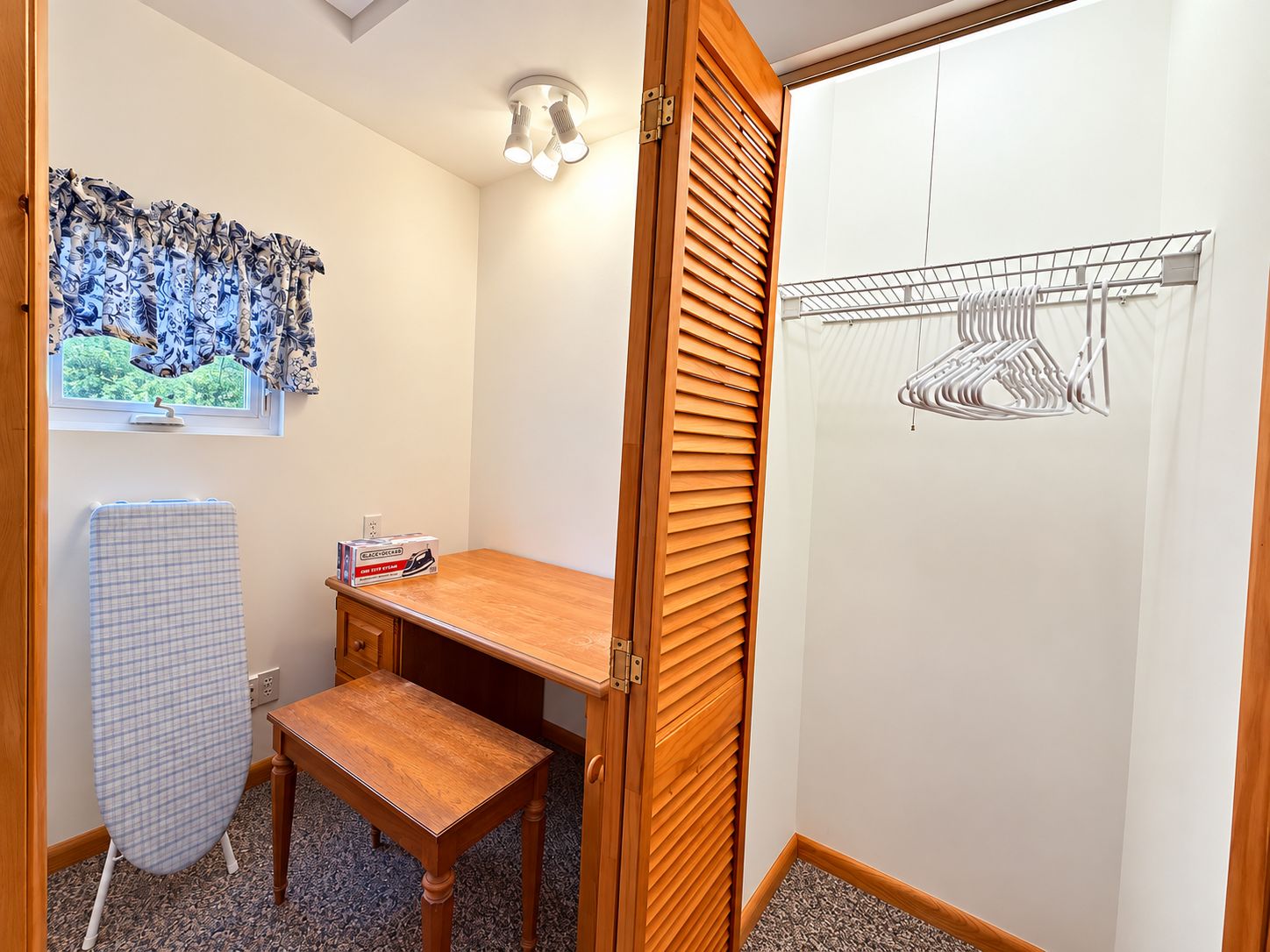 A room with a wooden desk, an ironing board, a radiator, and a wall-mounted drying rack.