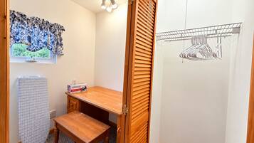 A room with a wooden desk, an ironing board, a radiator, and a wall-mounted drying rack.