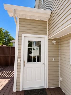 A white door with a glass panel, a brown deck, and beige siding on a house.
