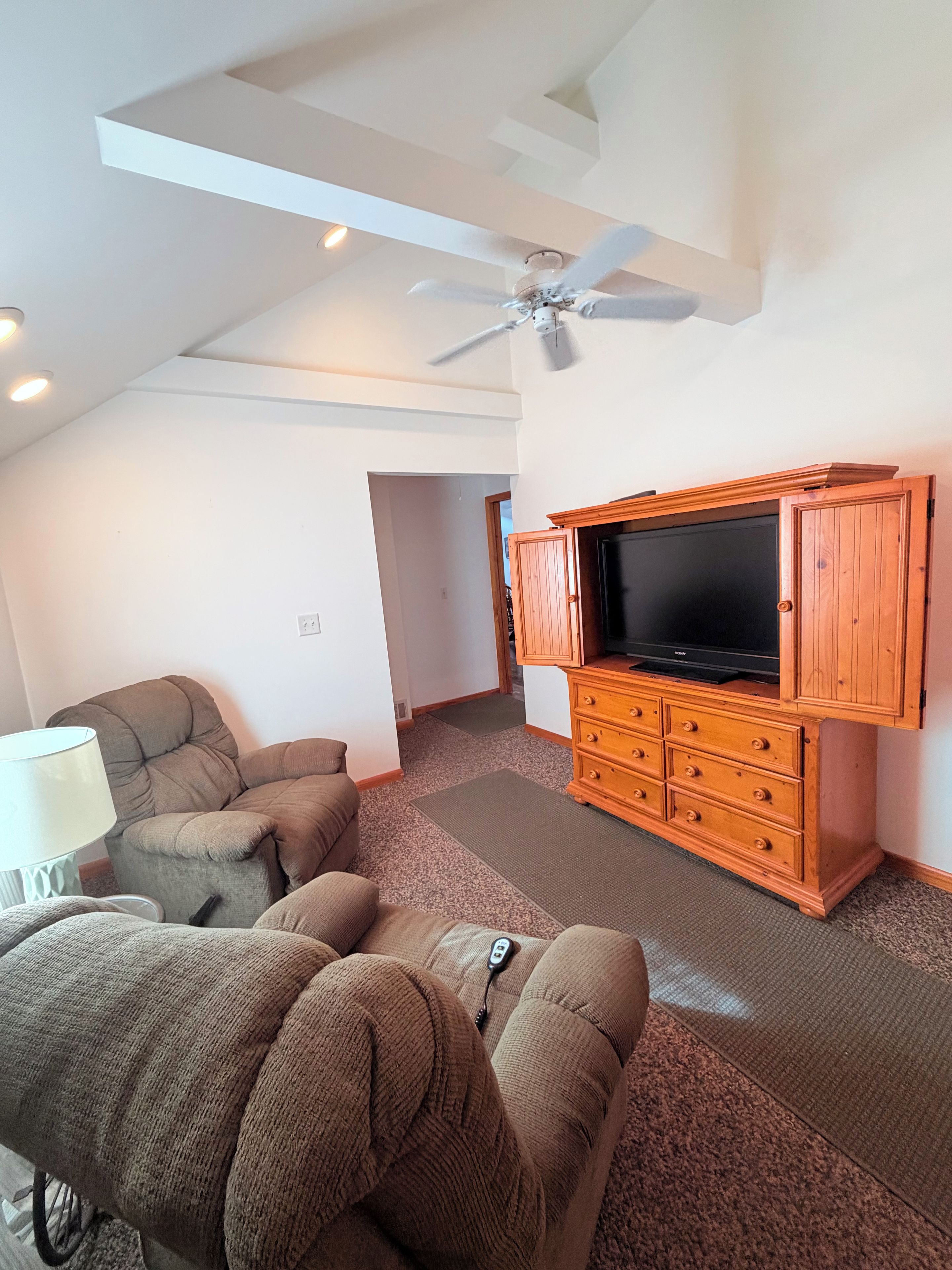 Un salon avec un ventilateur de plafond, un téléviseur posé sur un meuble en bois et un canapé marron.