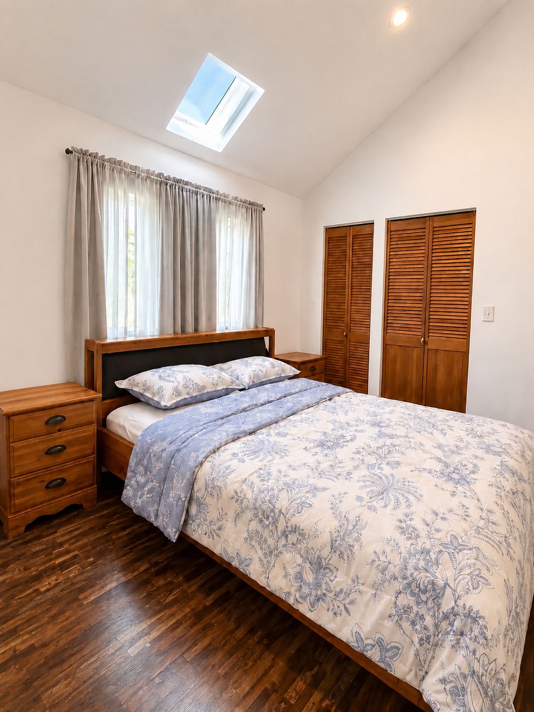 Une chambre à coucher avec un lit, des tables de chevet en bois, une lucarne et une armoire.