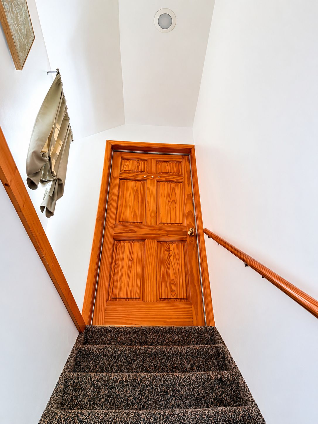 Une porte en bois se trouve en haut d’un escalier, avec une main courante sur le côté droit.