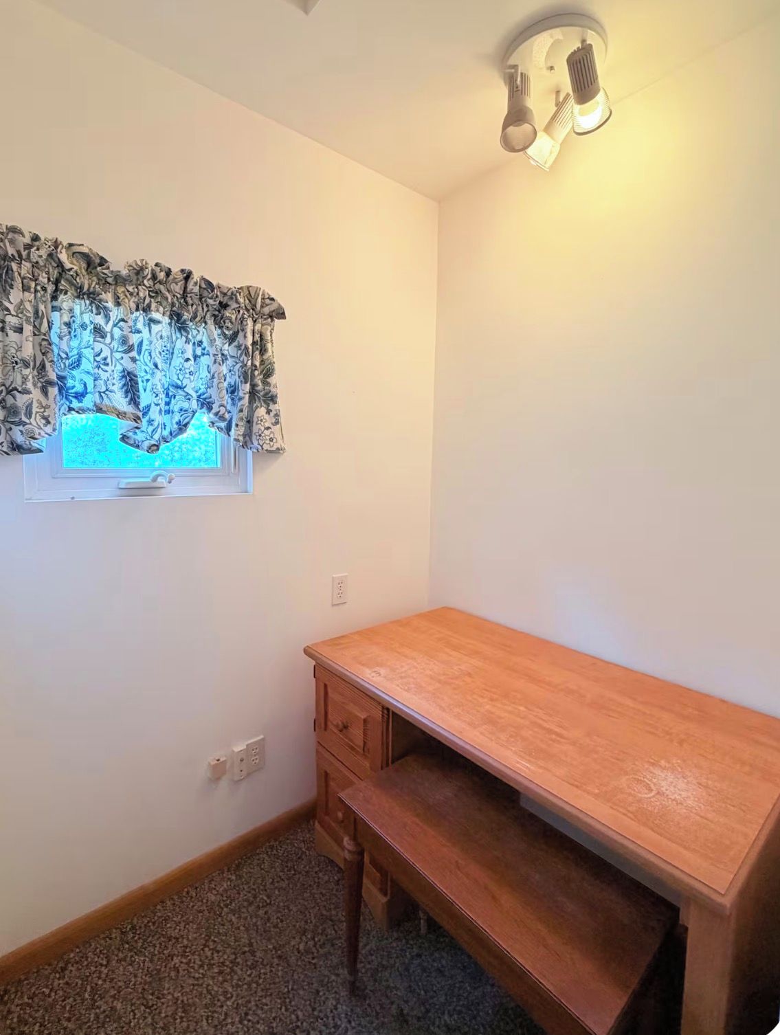 Une pièce avec une fenêtre, un bureau en bois, un banc et un luminaire au plafond.