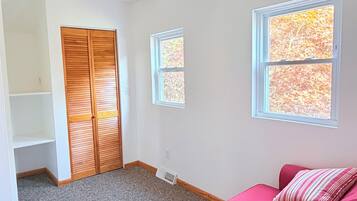 Ein Zimmer mit Deckenventilator, Schrank, Fenster mit Herbstlaub und einem roten Sofa.