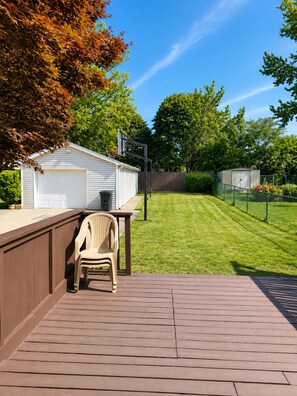 A backyard with a wooden deck, a white shed, and a green lawn.