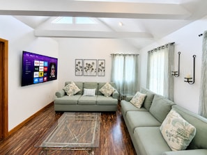 A modern living room with a flat-screen TV mounted on the wall, a sofa set, a glass coffee table, and a wooden floor.
