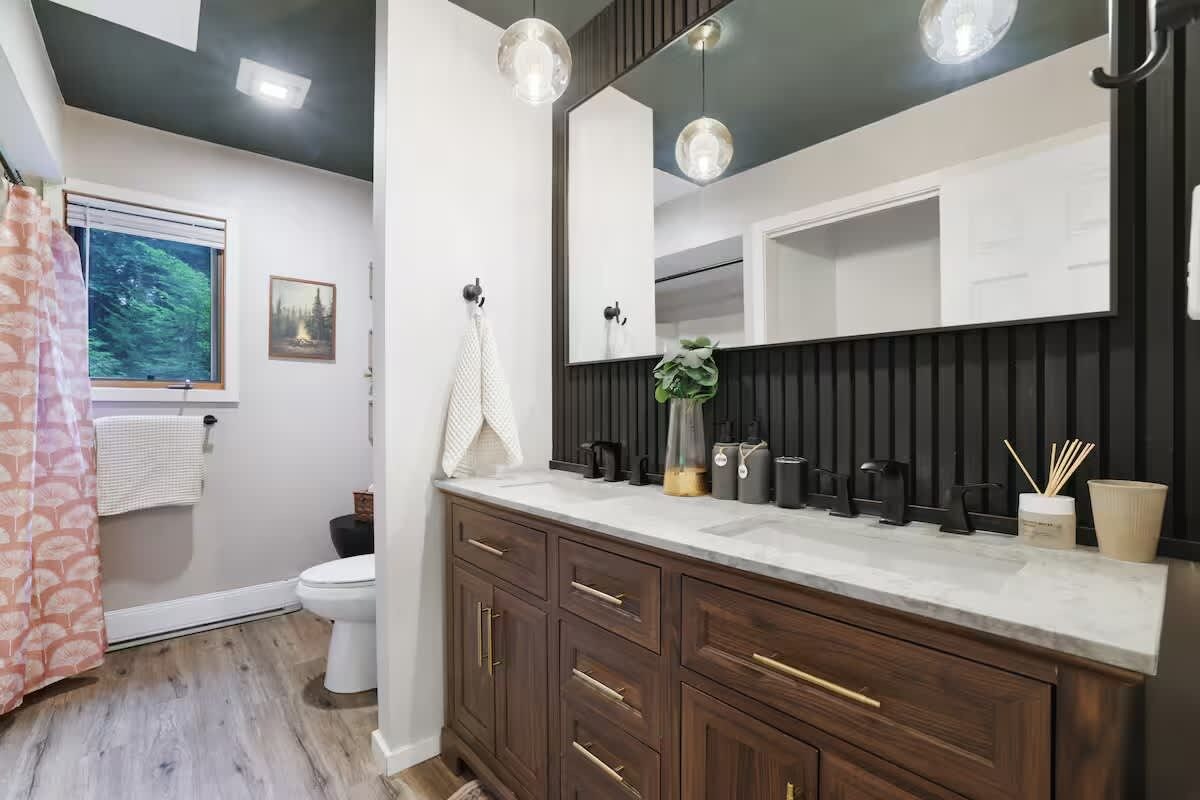 A modern bathroom with a large mirror, dark wood cabinets, and a white countertop.