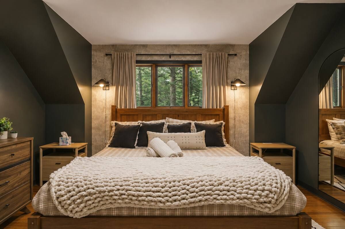 A bedroom with a large bed, wooden headboard, two bedside tables, a nightstand, a window with curtains, and a mirror on the wall.