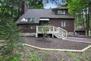 A wooden cabin with a deck, surrounded by trees. - Pine & Peace Retreat | Hot Tub | Fire Pit (Blakeslee)