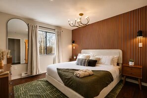 Ein Schlafzimmer mit einem großen Bett, einem Spiegel, einem Fenster mit Vorhängen, einer Holzvertäfelung und einem Nachttisch mit einer Lampe.