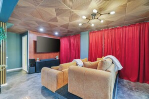 A home theater room with a large flat-screen TV, red curtains, and a sofa with a fur throw. - Putting Green | Hot Tub | Sauna | Theater | Arcade (Coolbaugh Township)