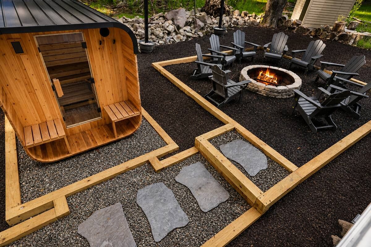 A wooden sauna structure with a fire pit and Adirondack chairs arranged around it.