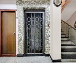Una puerta de madera, un portón de metal con diseño de rombos y una escalera con barandilla de vidrio.