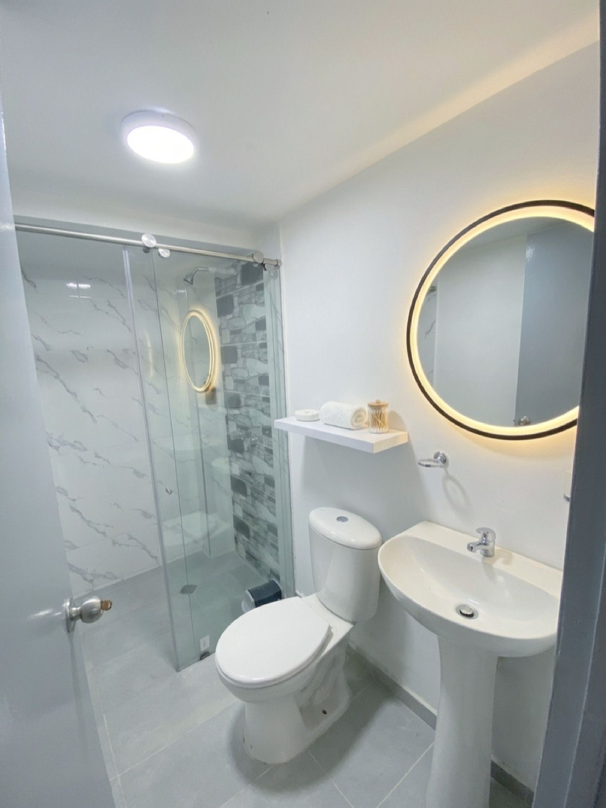 A modern bathroom with a glass-enclosed shower, a toilet, and a sink with a mirror.