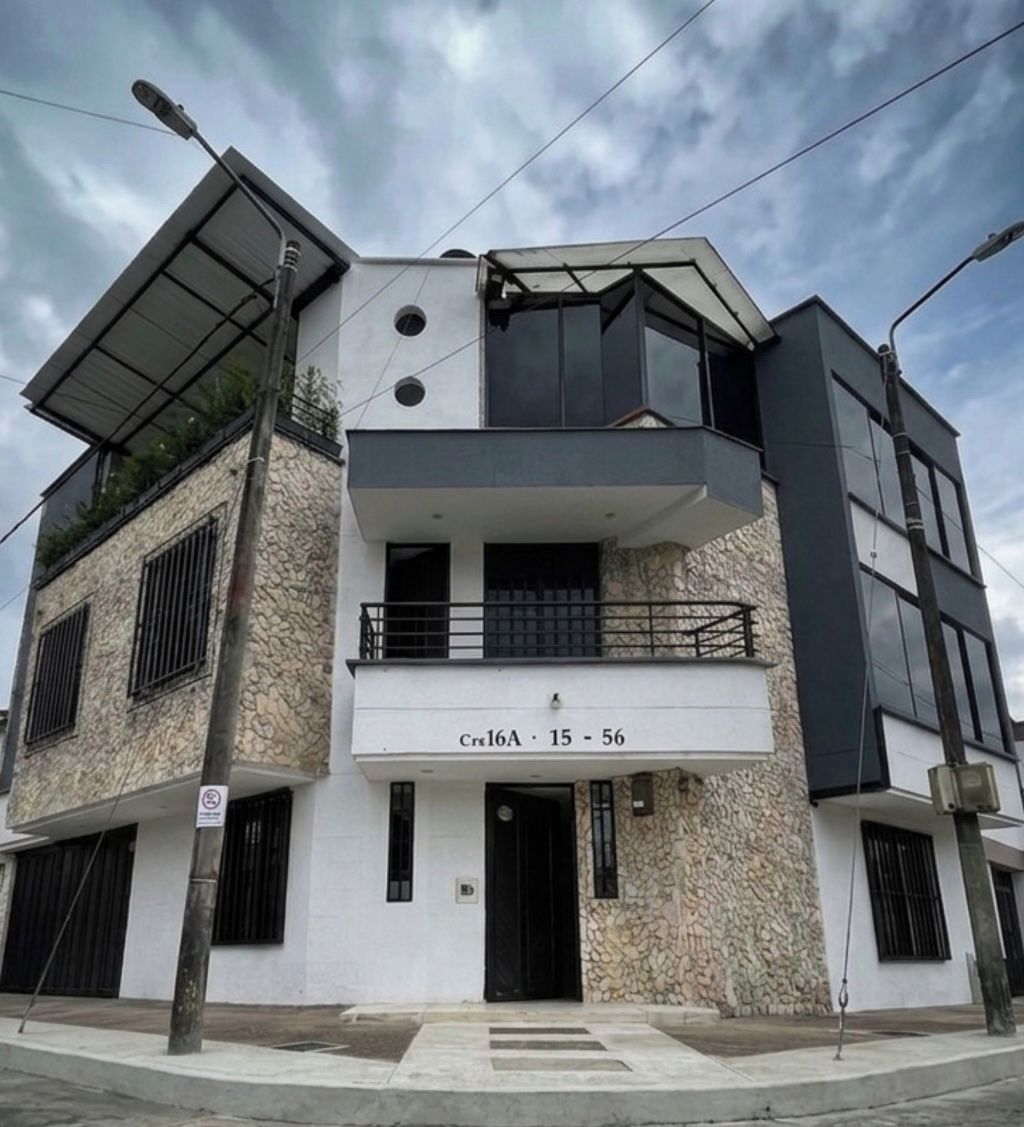 A modern two-story building with a flat roof, a balcony on the upper floor, and a ground-level entrance.
