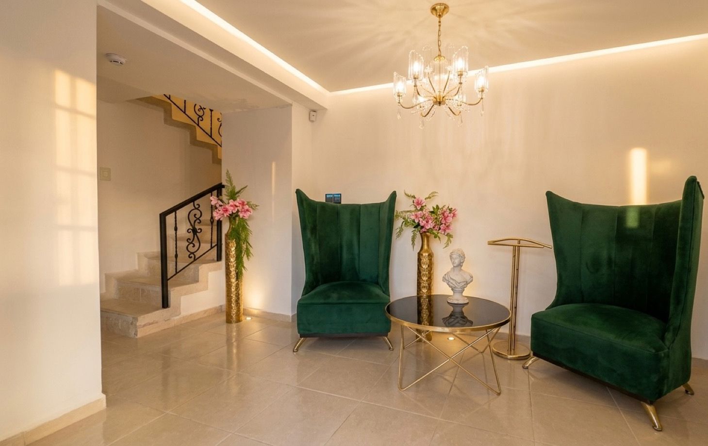 Uma sala de estar moderna com escada, poltronas de veludo verde, uma mesa de centro redonda e um candelabro.