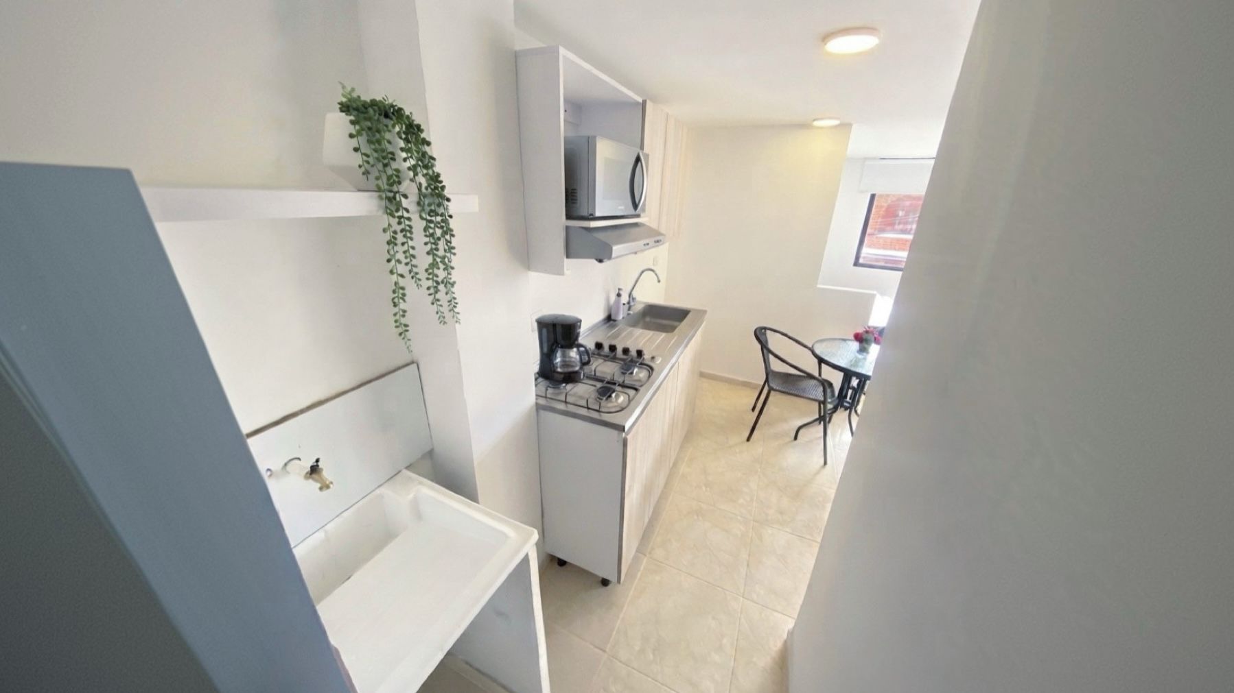 Una cocina compacta con estufa a gas, microondas y pileta. Hay un pequeño comedor con una mesa y sillas.
