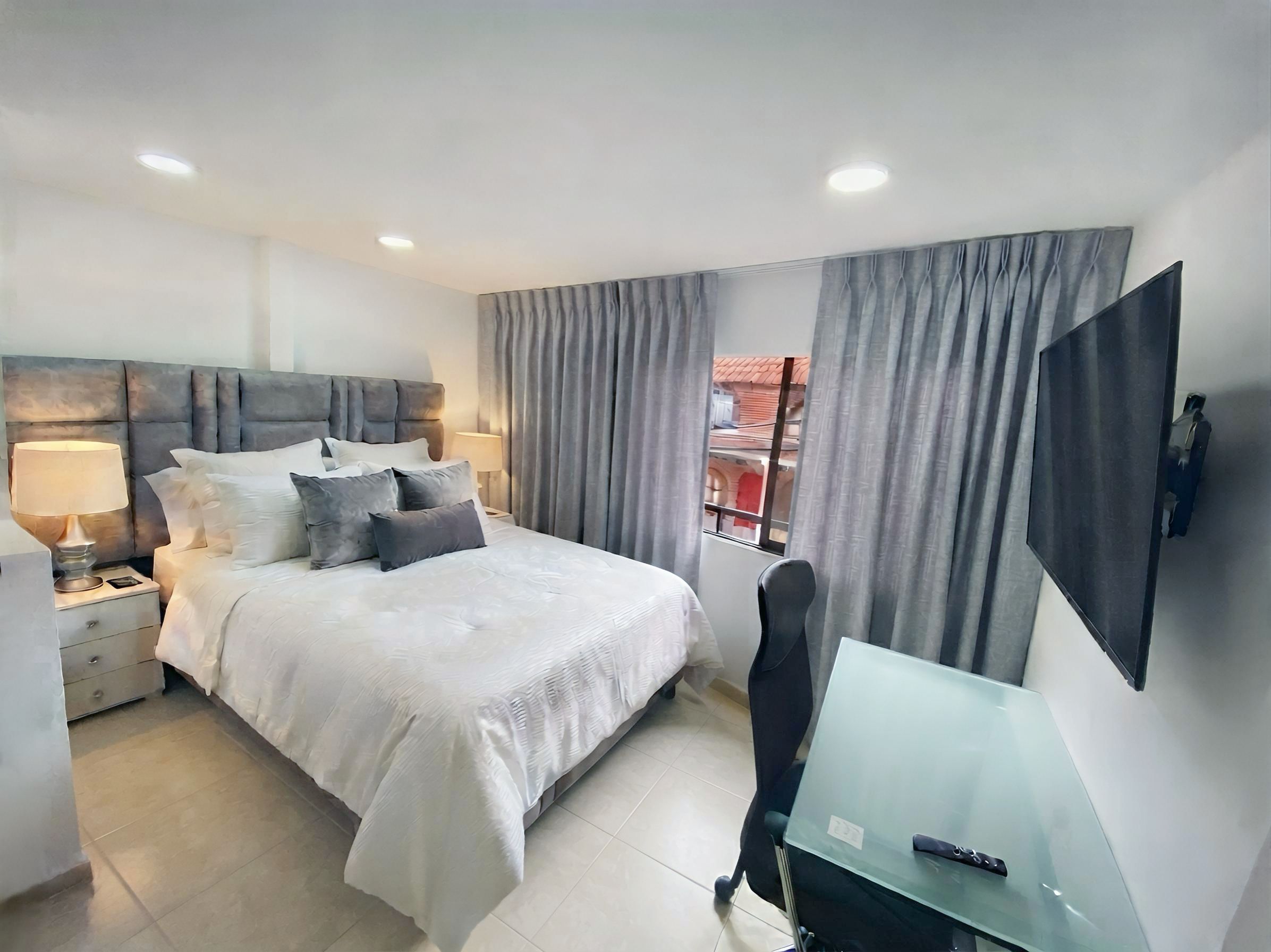 A modern bedroom with a bed, bedside tables, a desk, a chair, and a TV.