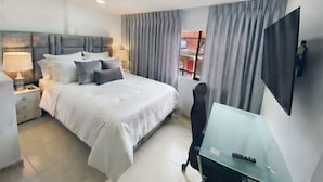 Quarto moderno com cama, mesas de cabeceira, escrivaninha, cadeira e televisão.