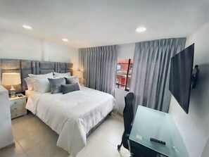 A modern bedroom with a bed, bedside tables, a desk, a chair, and a TV. - New modern studio apartment in Dosquebradas, Pereira (Dosquebradas)