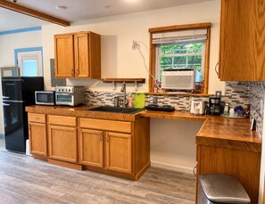 A kitchen with wooden cabinets, a black refrigerator, a microwave, an oven, and a window with blinds. - Nashville's Famous Loveless Cafe Stay (Nashville)