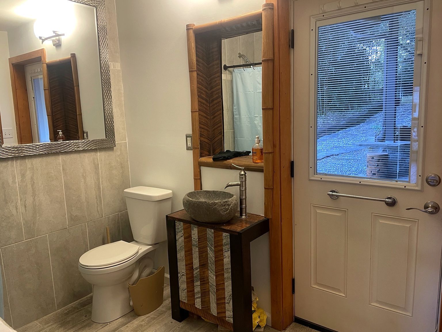 A bathroom with a toilet, a stone sink, a mirror, and a window with blinds.