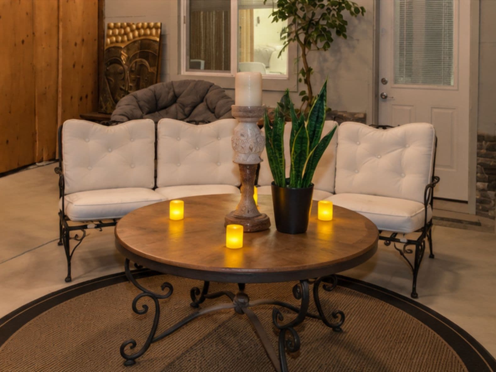 A round wooden table with a candle centerpiece, surrounded by two white cushioned sofas with black metal legs.