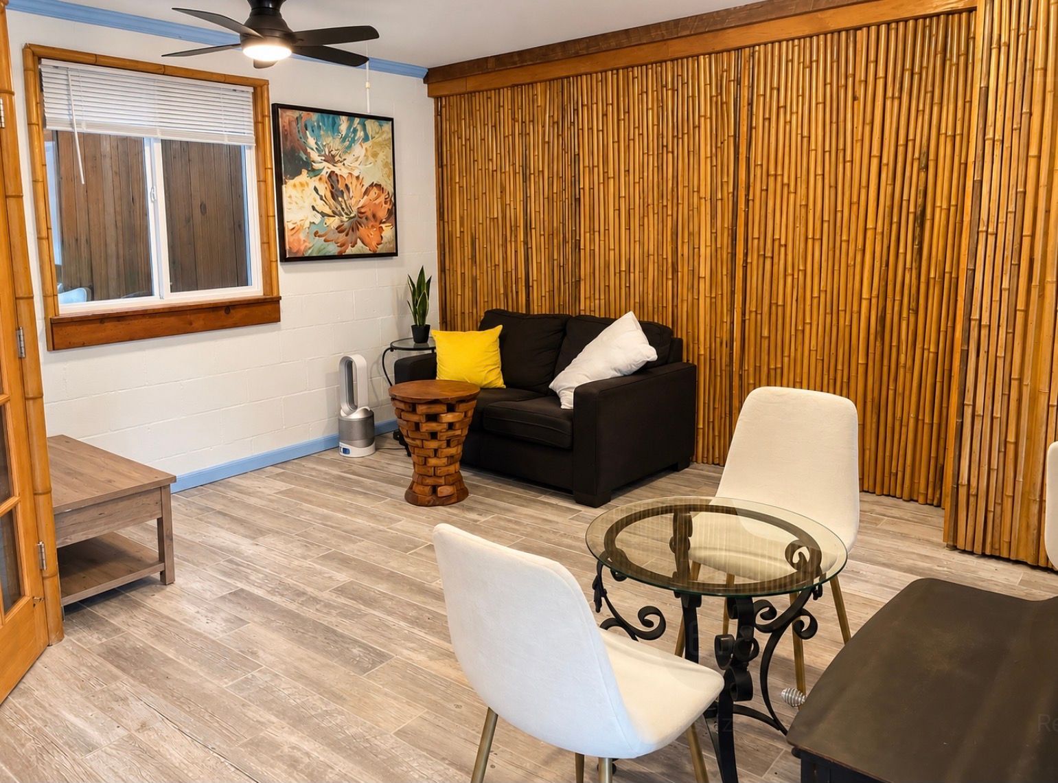 Een woonkamer met een zwarte bank, een glazen salontafel en een witte fauteuil.