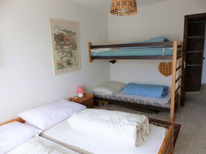 A bunk bed room with a single bed on the bottom and a bunk bed above. There is a nightstand with a lamp, a framed picture on the wall, and a door to the right. - Flurina / Burtscher, (Falera). 3 Zimmerferienwohnung für max. 4 Personen, am ge by Interhome (Falera)