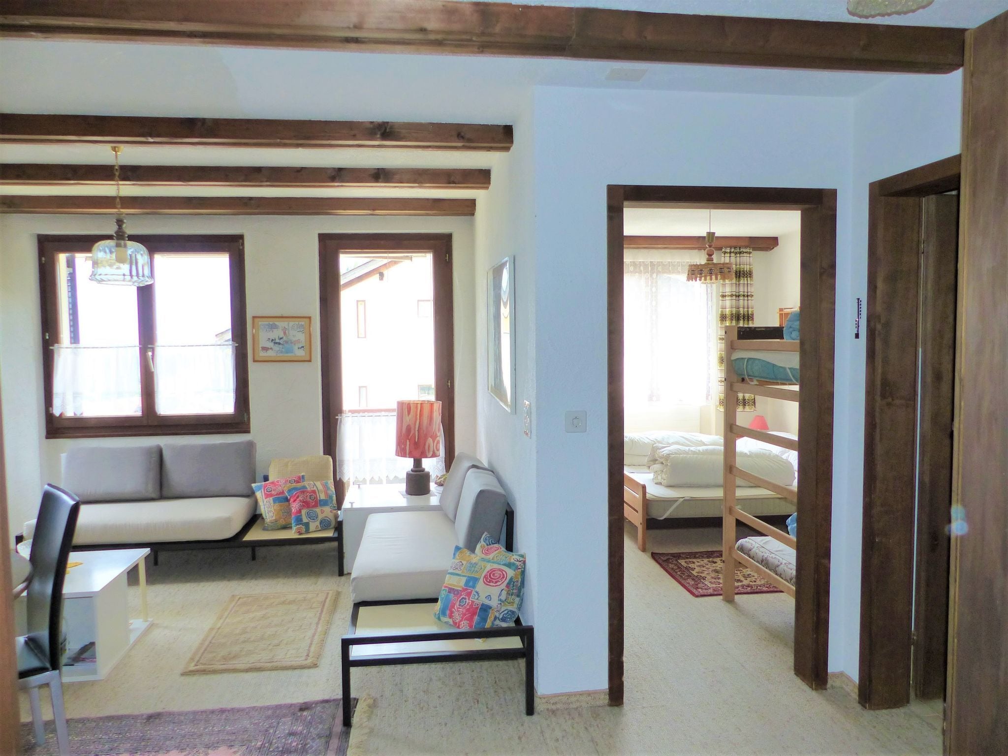 A room with a sofa, a chair, a desk, a bed with a bunk, and a window with curtains.