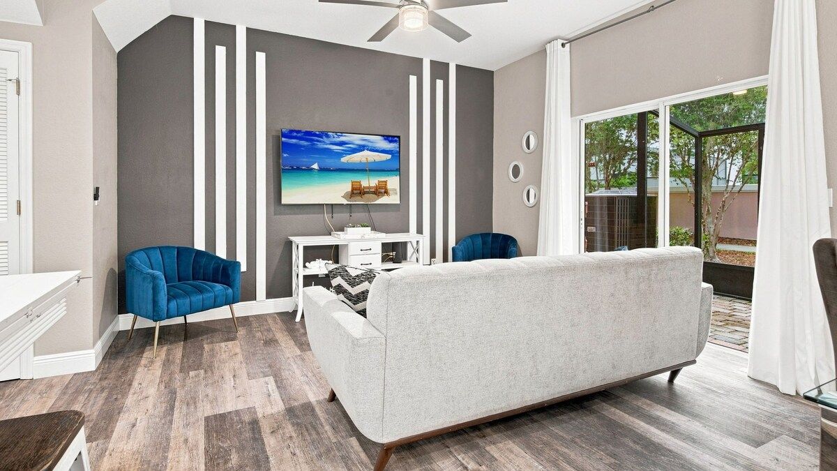 A modern living room with a grey sofa, blue chairs, a white desk, and a TV mounted on the wall.