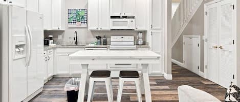 Una cocina moderna con armarios blancos, una isla central y un comedor con dos taburetes.