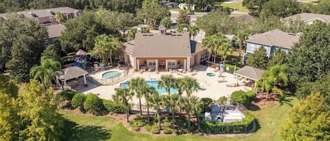 A residential area with a large house featuring a swimming pool, surrounded by lush greenery and a body of water.