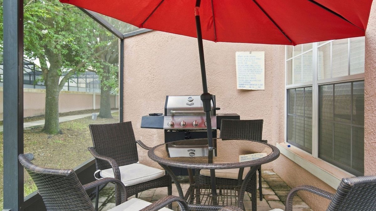 An outdoor patio with wicker furniture, a grill, and a red umbrella.