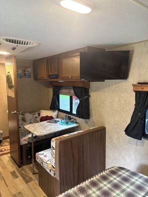 Interior compacto de una autocaravana con kitchenette, cama y televisor montado.