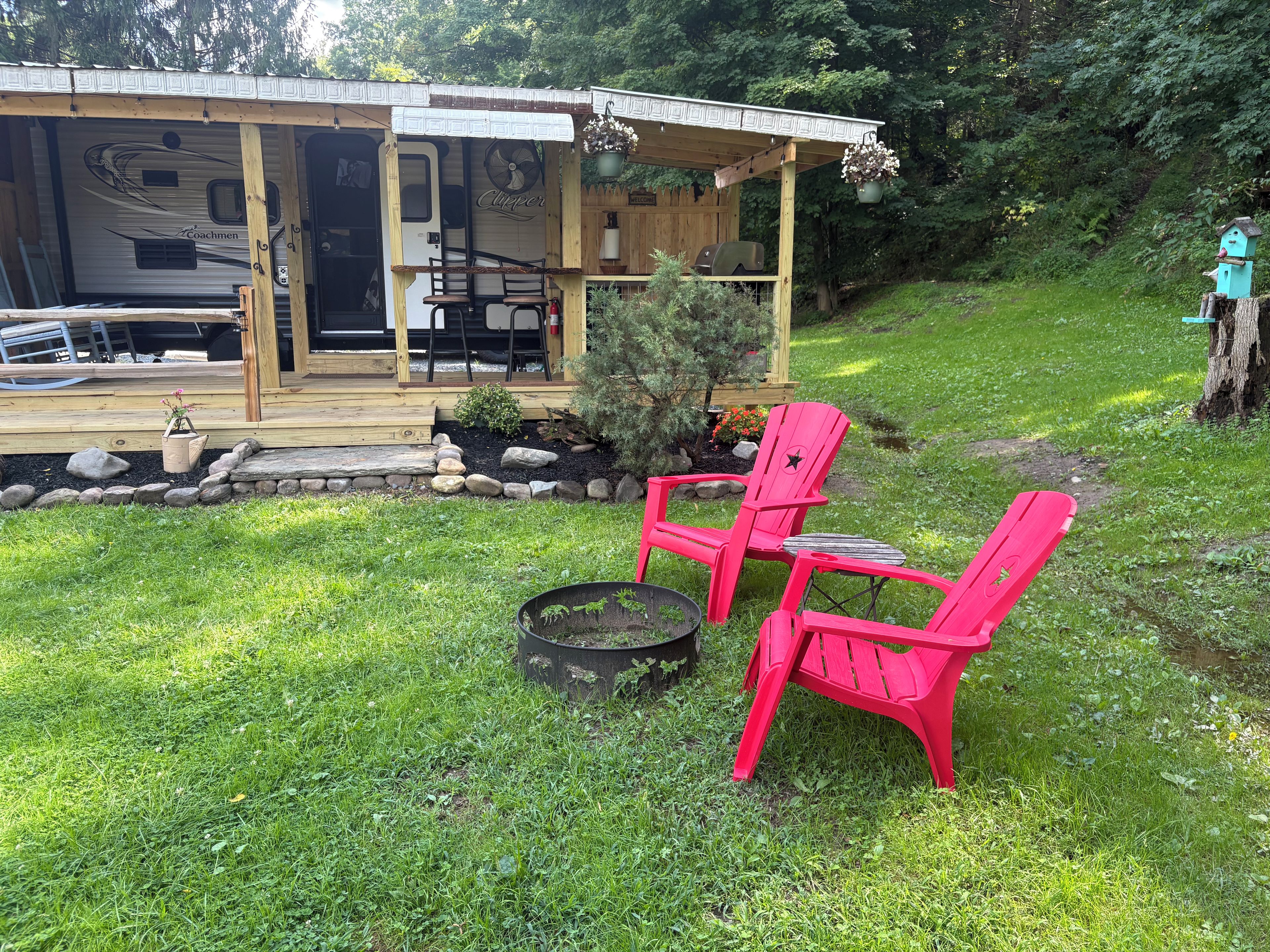 Puinen terassi, jossa on katettu oleskelualue, nuotiopaikka sekä pieni kivien ja kasvien koristama puutarha.