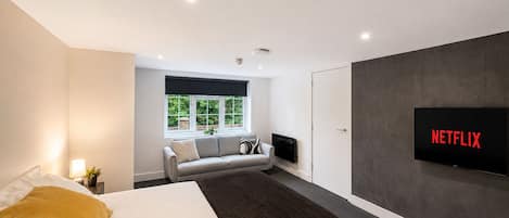 A modern bedroom with a bed, a sofa, a TV, and a window with a view.